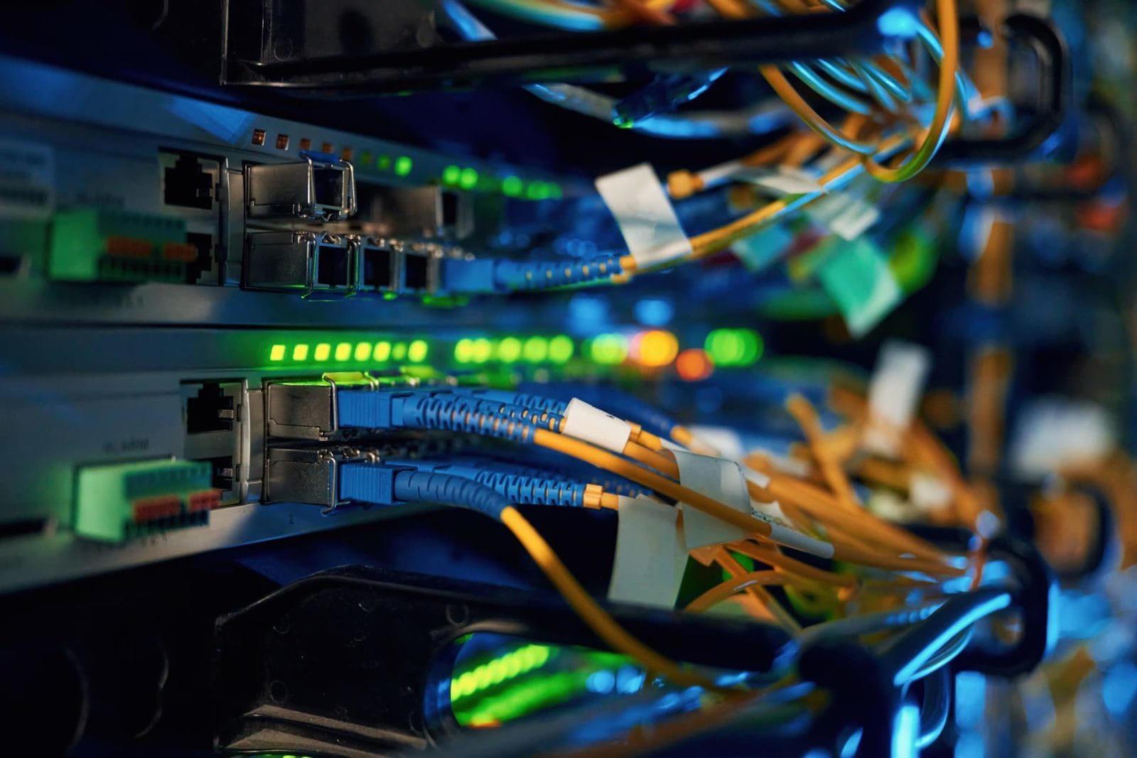 Close-up of blue and orange fiber patch cables connected to network switches in a lit server rack